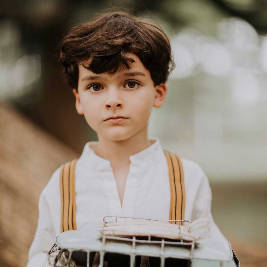 Young boy holding a vintage toy plane outdoors, wearing a white shirt and suspenders.