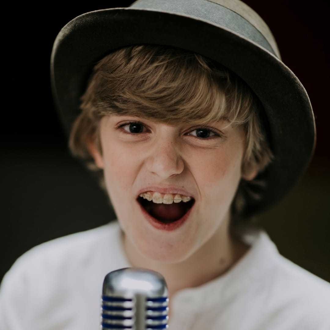 Young boy singing passionately into a vintage microphone, wearing a hat.