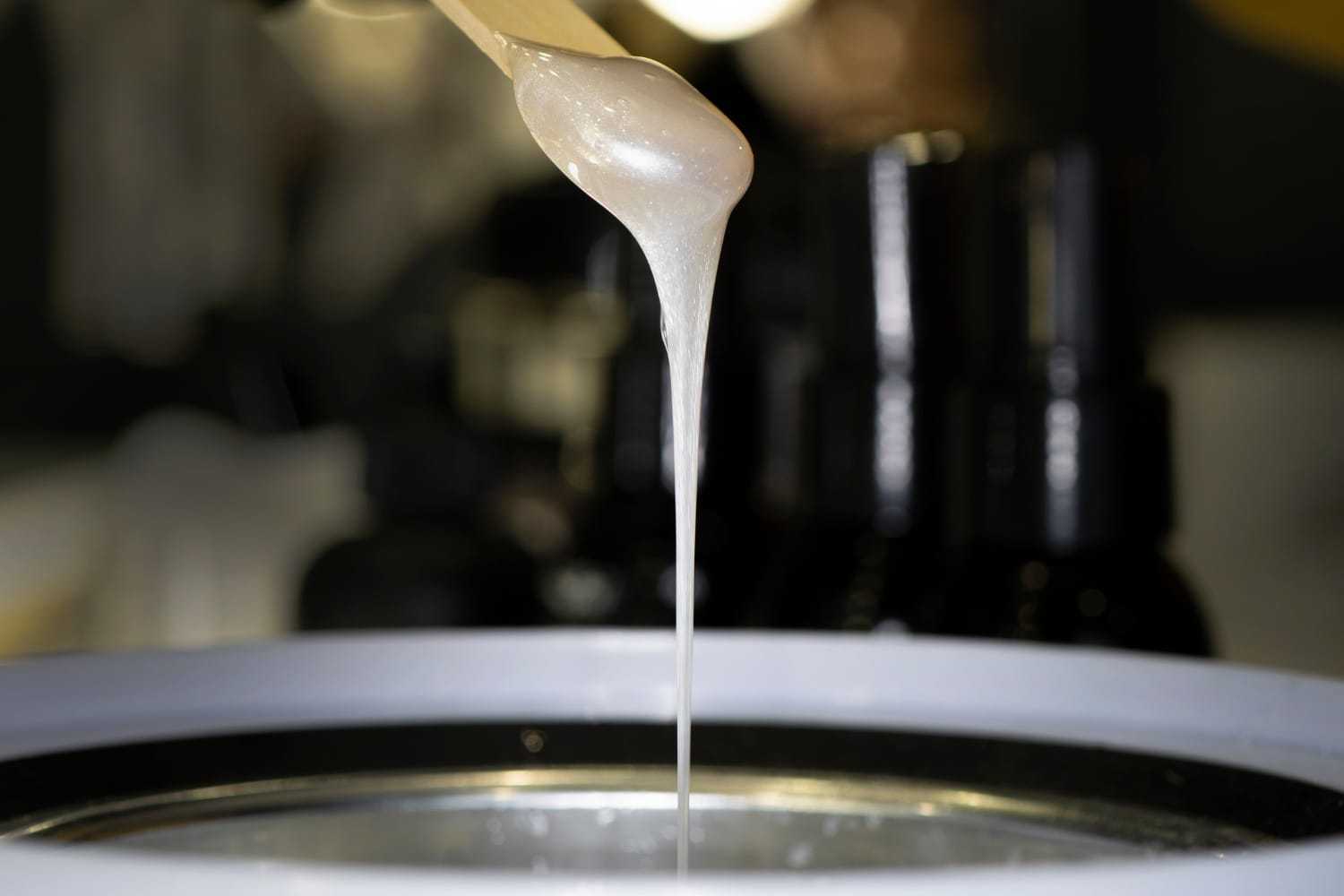 Hot wax dripping from stick into pot, ready for hair removal treatment.